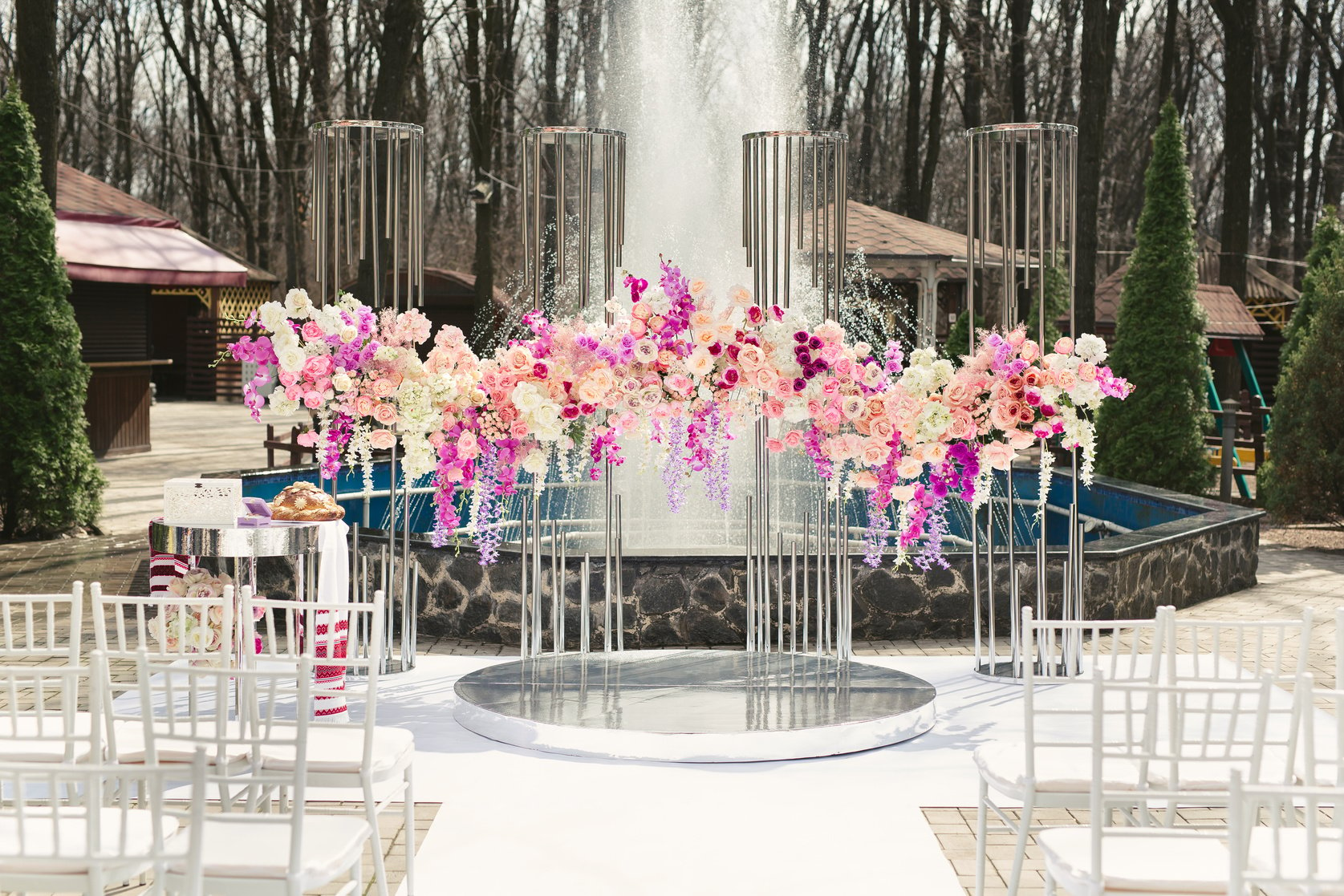 Wedding arch decorated with pink and white flowers standing in the luxury area of the wedding ceremony with fountain